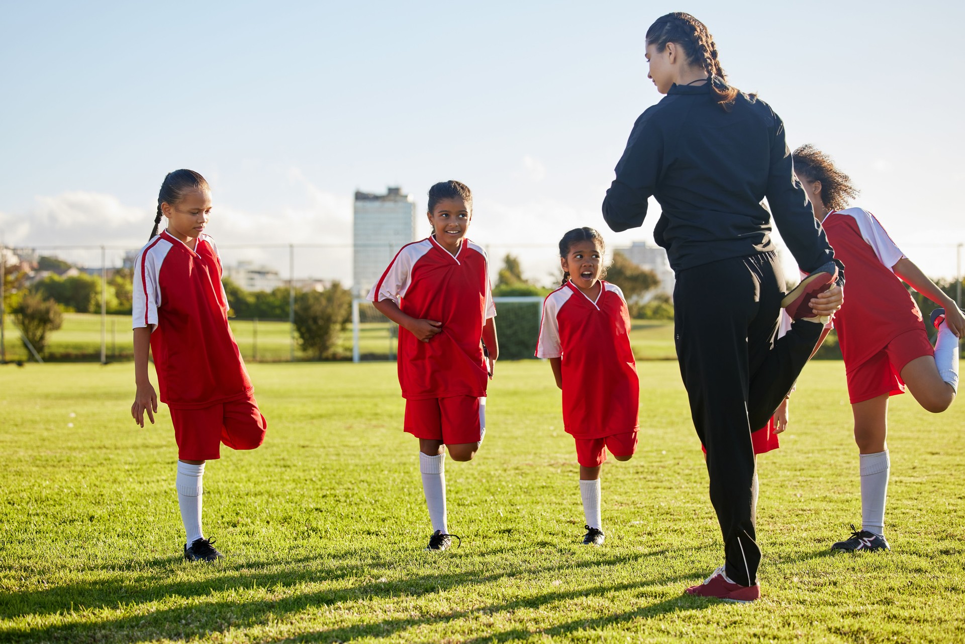 Team, soccer and girls stretching in football stadium with coach in training, sports and group warm up together. Healthy, teamwork and young school children doing exercise with fitness instructor